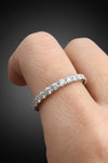 Digital photograph of a shimmering diamond eternity band worn on a finger featuring a continuous row of round brilliant-cut diamonds and a delicate shared-prong setting against a dark gradient background