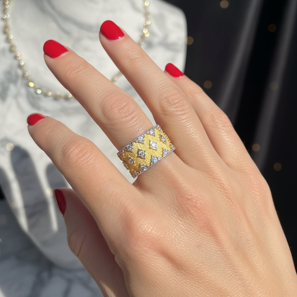 Photograph of a Buccellati wide gold band ring on a hand with bright red nail polish featuring textured yellow gold and pavé diamonds against a blurred background with a marble bust and dark curtain