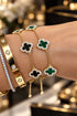 Gold bracelet with clover-shaped charms on a wrist against a neutral background