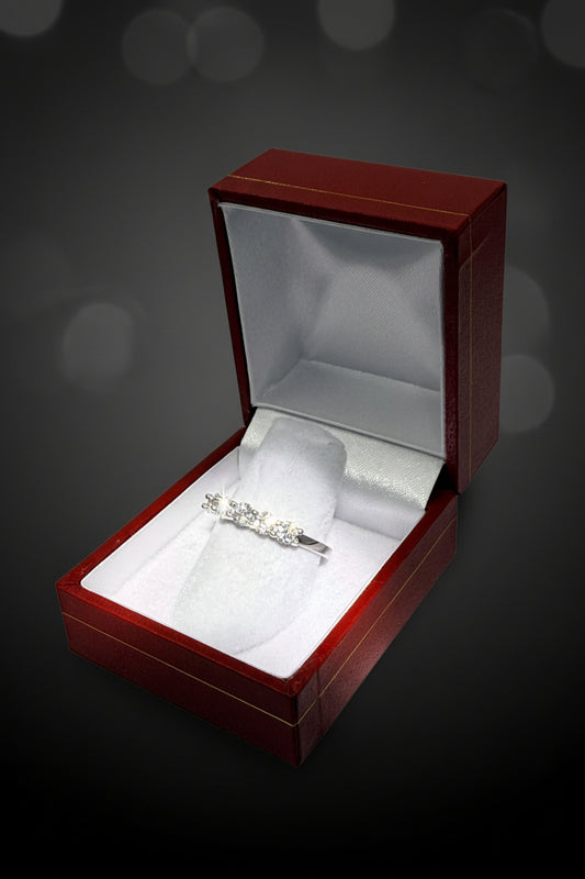 Studio photograph of a radiant five-stone diamond ring showcased in an open red jewelry box featuring a gold-lined lid and a white satin interior against a dark bokeh background