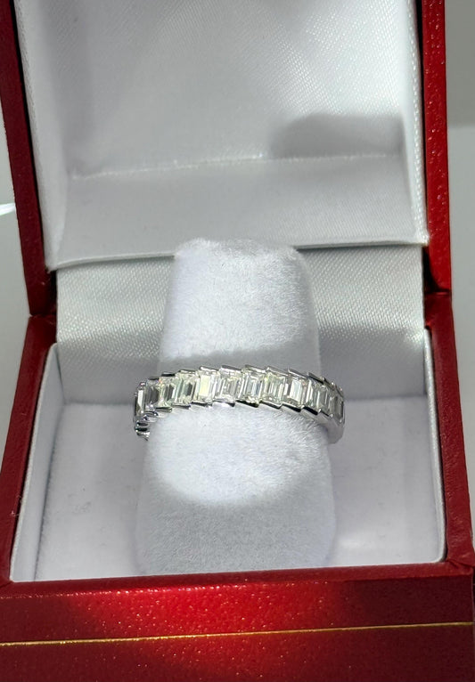 Photograph of a brilliant emerald-cut diamond eternity band displayed on a white velvet pedestal inside a signature red jewelry box with a white satin-lined interior and a polished silver-toned metal setting