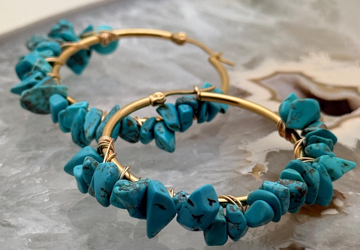 Handcrafted wire-wrapped jewelry featuring turquoise chip gold hoop earrings resting on a polished crystalline agate geode surface showcasing vibrant blue stones with dark matrix veining and intricate golden wire work