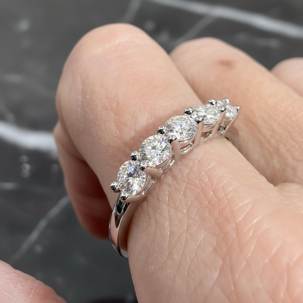 Macro photograph of a five-stone diamond anniversary ring worn on a hand against a black marble surface featuring brilliant round-cut stones in a shared-prong white gold setting with a high-polish finish and light-catching facets