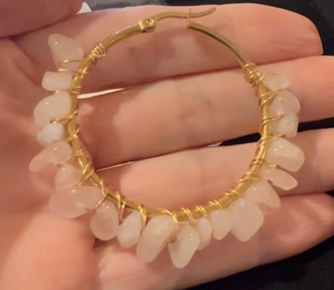 Handmade gold wire-wrapped hoop earring held in a palm featuring raw pale pink rose quartz chips and a thin circular metallic frame