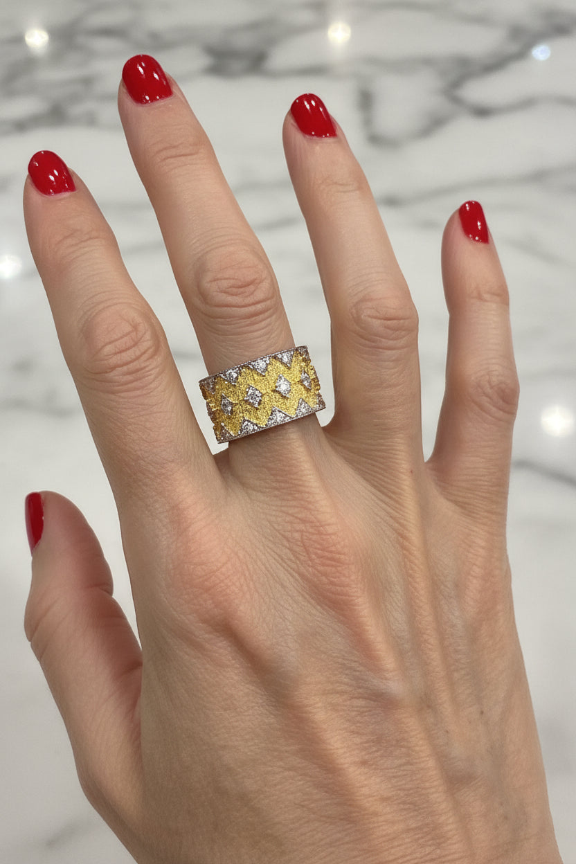 Photograph of a luxury yellow gold honeycomb wide band ring set with sparkling white diamonds worn on a hand with vibrant red manicured nails against a polished white marble surface