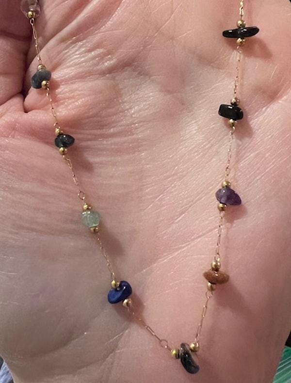 Handmade jewelry necklace featuring a delicate gold-tone chain with tiny spacer beads and colorful tumbled gemstone chips in purple amethyst and deep blue lapis lazuli held in a human palm