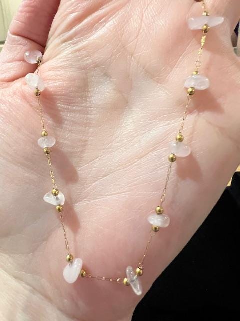 Handmade rose quartz and gold gemstone necklace held in the palm of a hand featuring a delicate link chain with small gold bead accents and translucent irregularly shaped pale pink stone chips