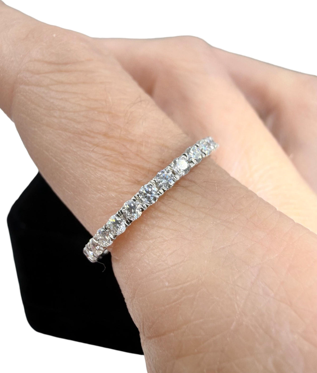 Photograph of a diamond eternity band on a finger featuring brilliant round-cut diamonds in a meticulous prong setting on a polished white metal band
