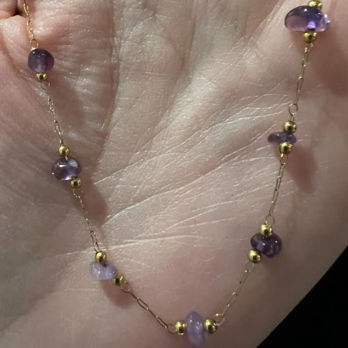 Gold and gemstone jewelry photograph of a delicate gold chain necklace featuring irregular purple amethyst chips and tiny gold spacer beads resting in a person's hand
