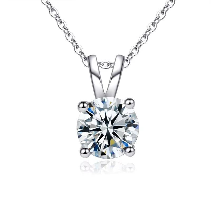Professional product photograph of a round brilliant-cut solitaire diamond pendant on a white background featuring a high-polish four-prong setting, a delicate silver cable chain, and shimmering blue and yellow prismatic light refractions