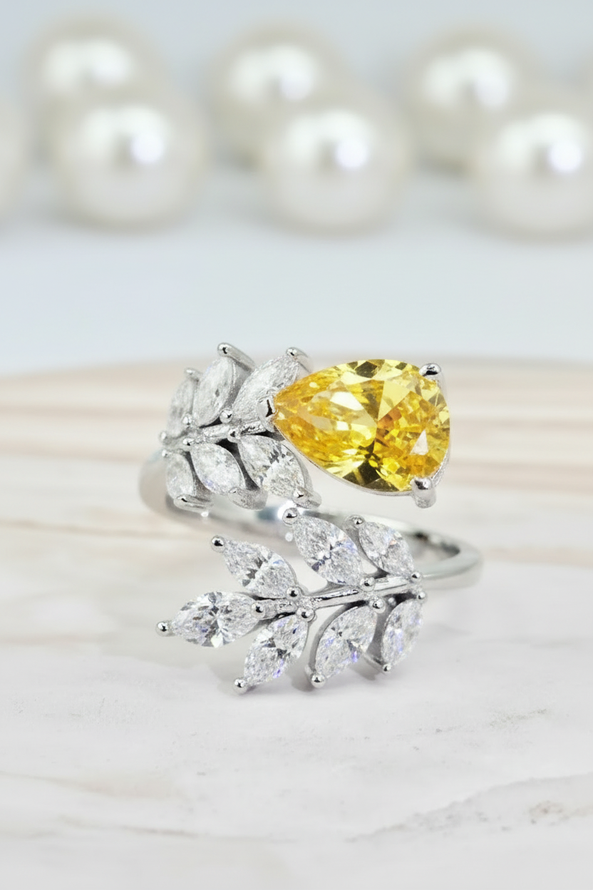 Ring with a yellow pear-shaped gemstone and leaf-shaped diamonds on a light background  - Ali & Eve Jewels