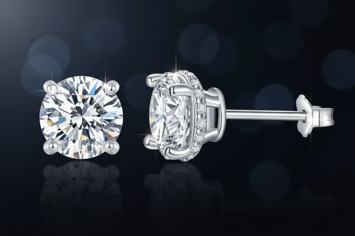 Commercial product photography of round brilliant-cut diamond stud earrings featuring a shimmering halo setting and butterfly clutch back displayed on a dark reflective surface with soft blue bokeh highlights