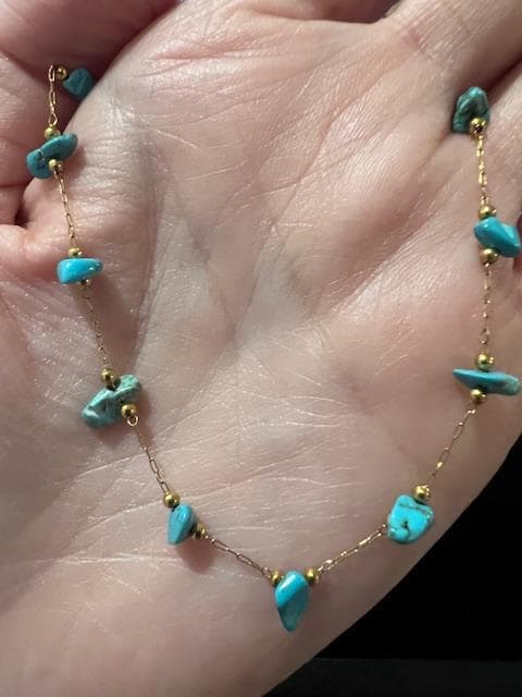 Gold and turquoise gemstone necklace featuring vibrant cyan chips and tiny gold-tone spacer beads on a delicate chain displayed against a human palm