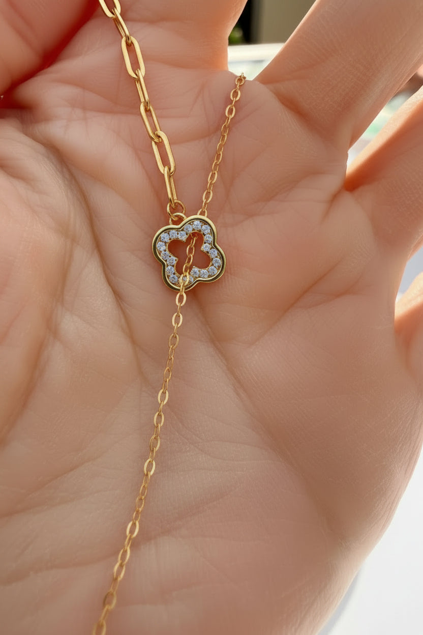Gold necklace with a clover -shaped pendant held in a hand.