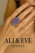 Hand wearing a purple ring with &