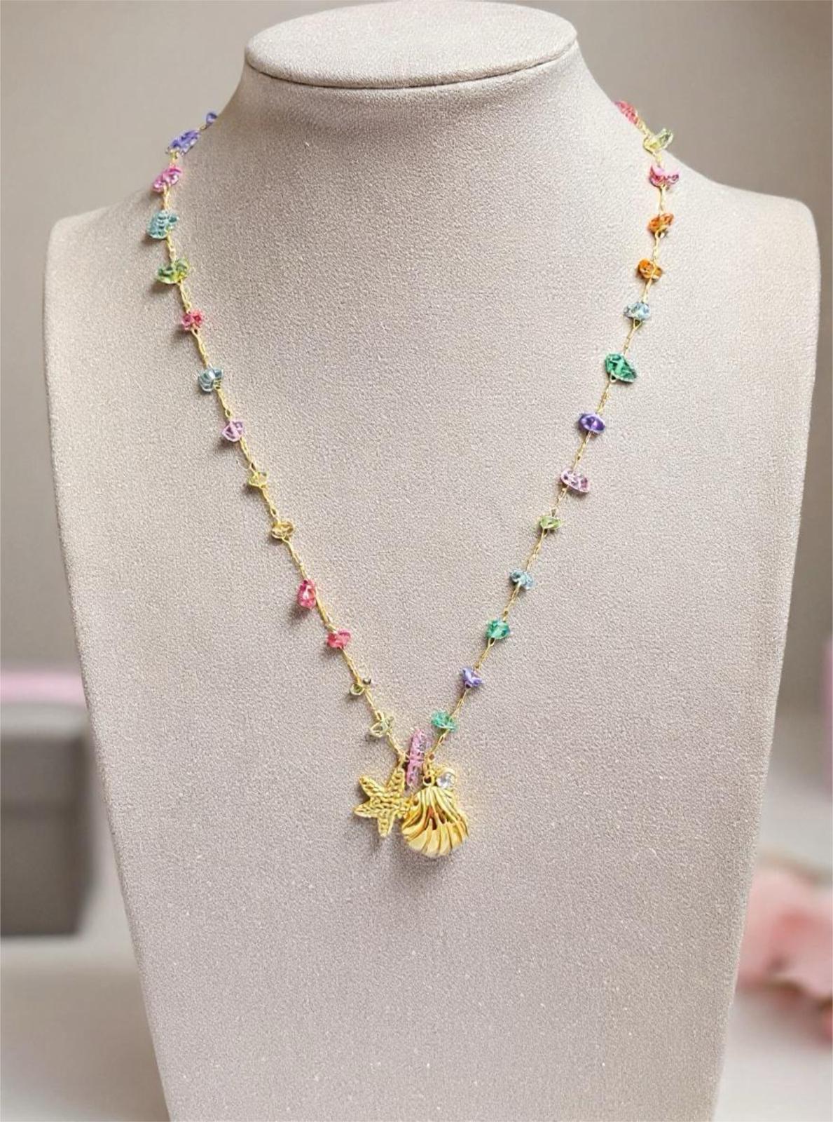 Gold jewelry necklace displayed on a gray mannequin bust featuring a gold starfish and seashell charm accented by multi-colored pastel beads and a delicate chain