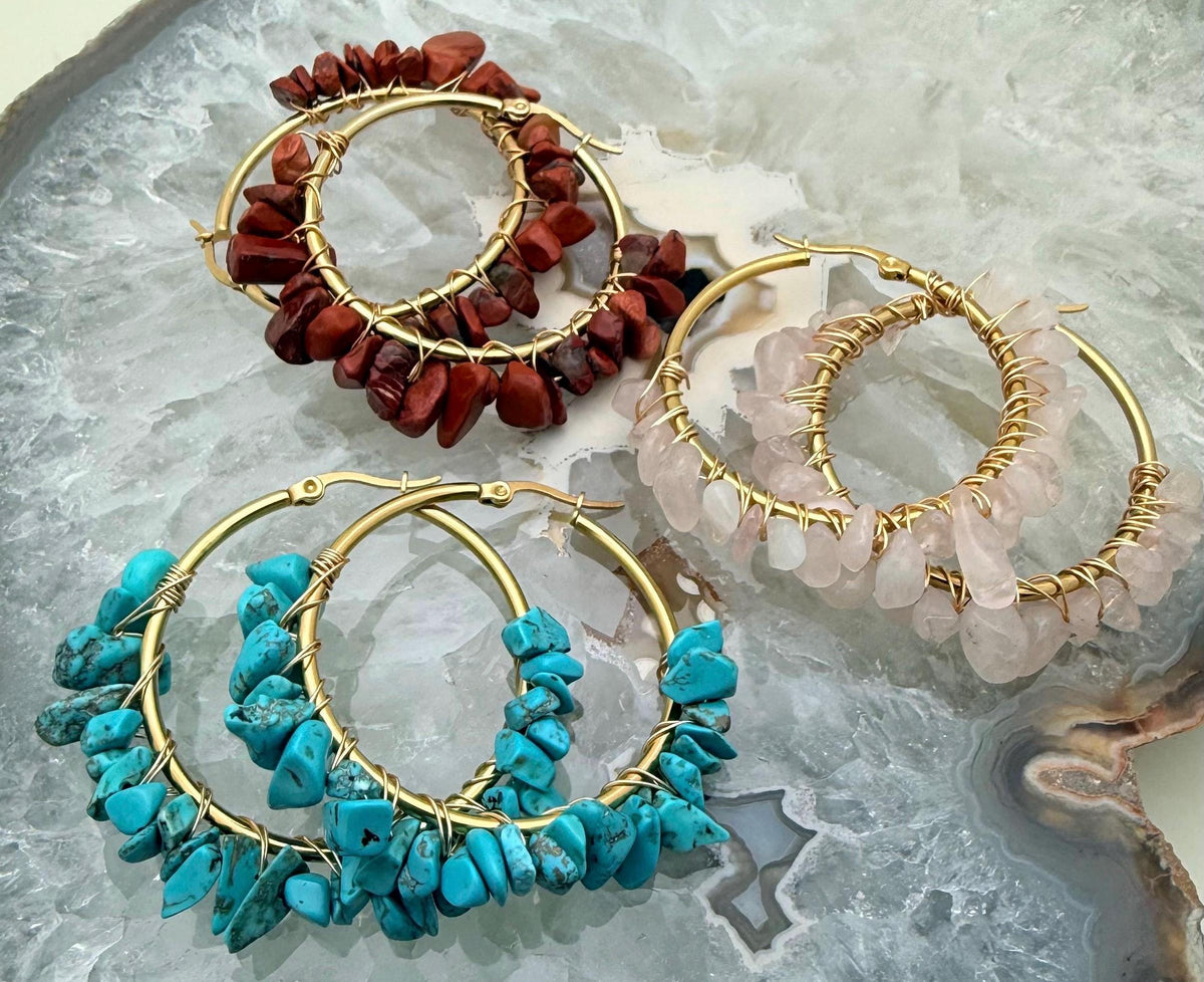Handcrafted wire-wrapped jewelry featuring three pairs of gold hoop earrings adorned with red jasper, turquoise, and rose quartz chips on a polished crystalline geode slice with intricate gold wire detailing and natural stone textures