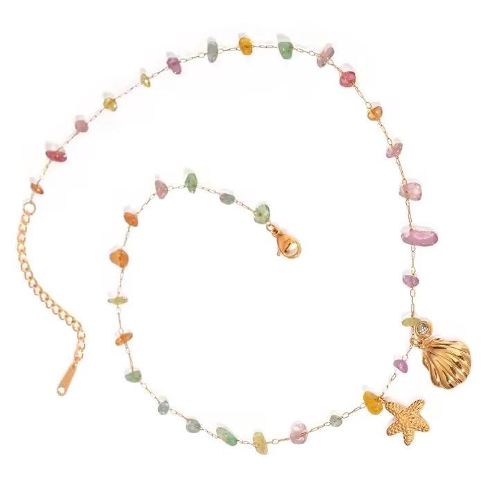 Gold and gemstone jewelry necklace featuring a delicate chain with multi-colored tumbled beads and nautical gold seashell and starfish charms set against a white background