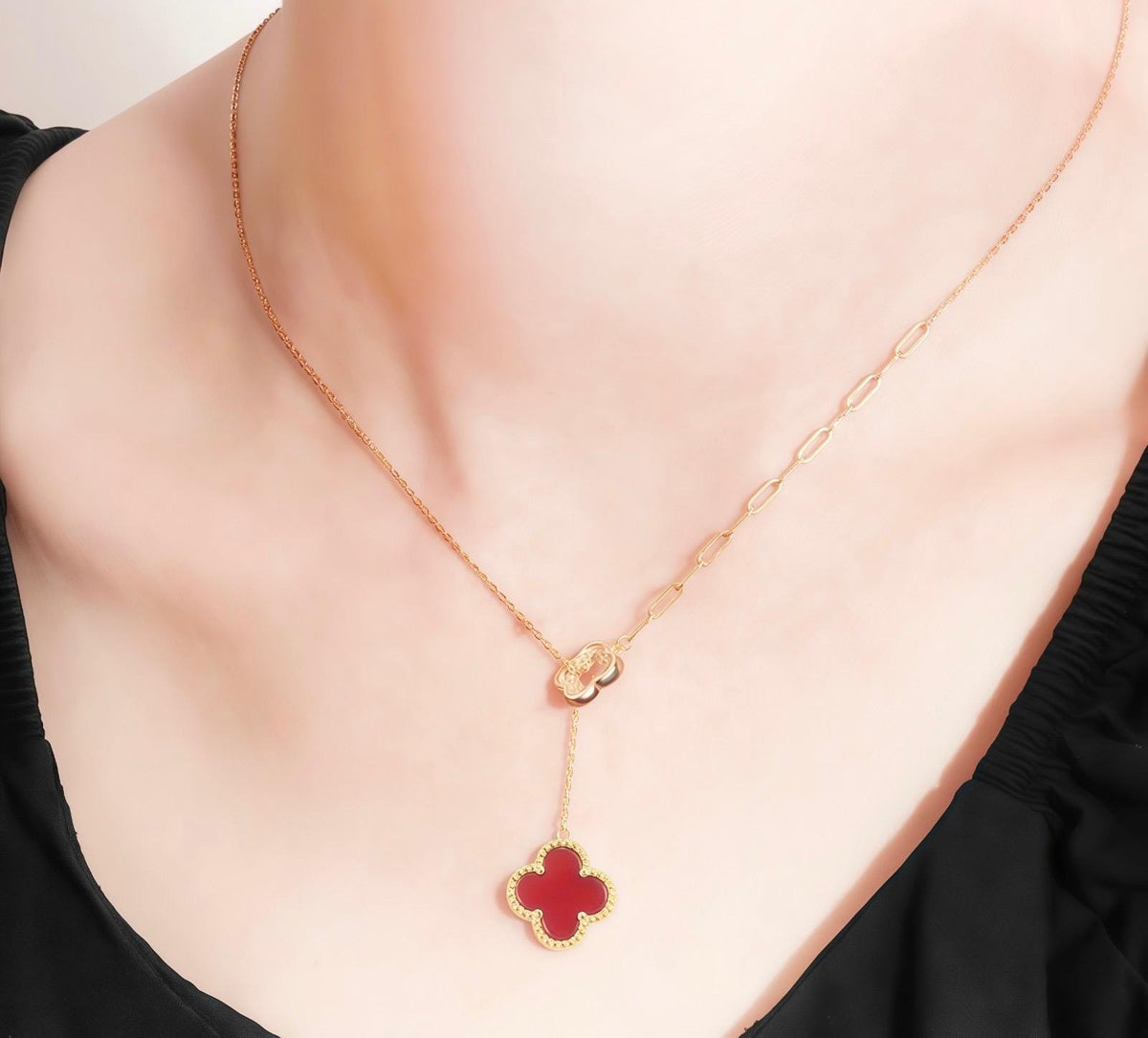 Gold necklace with a red agate clover  on a model wearing a black top.