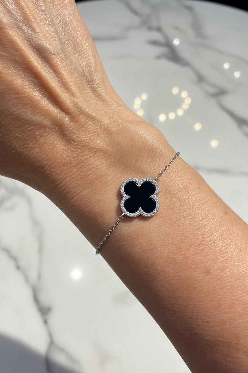 Silver bracelet with an onyx clover on a wrist against a marble background
