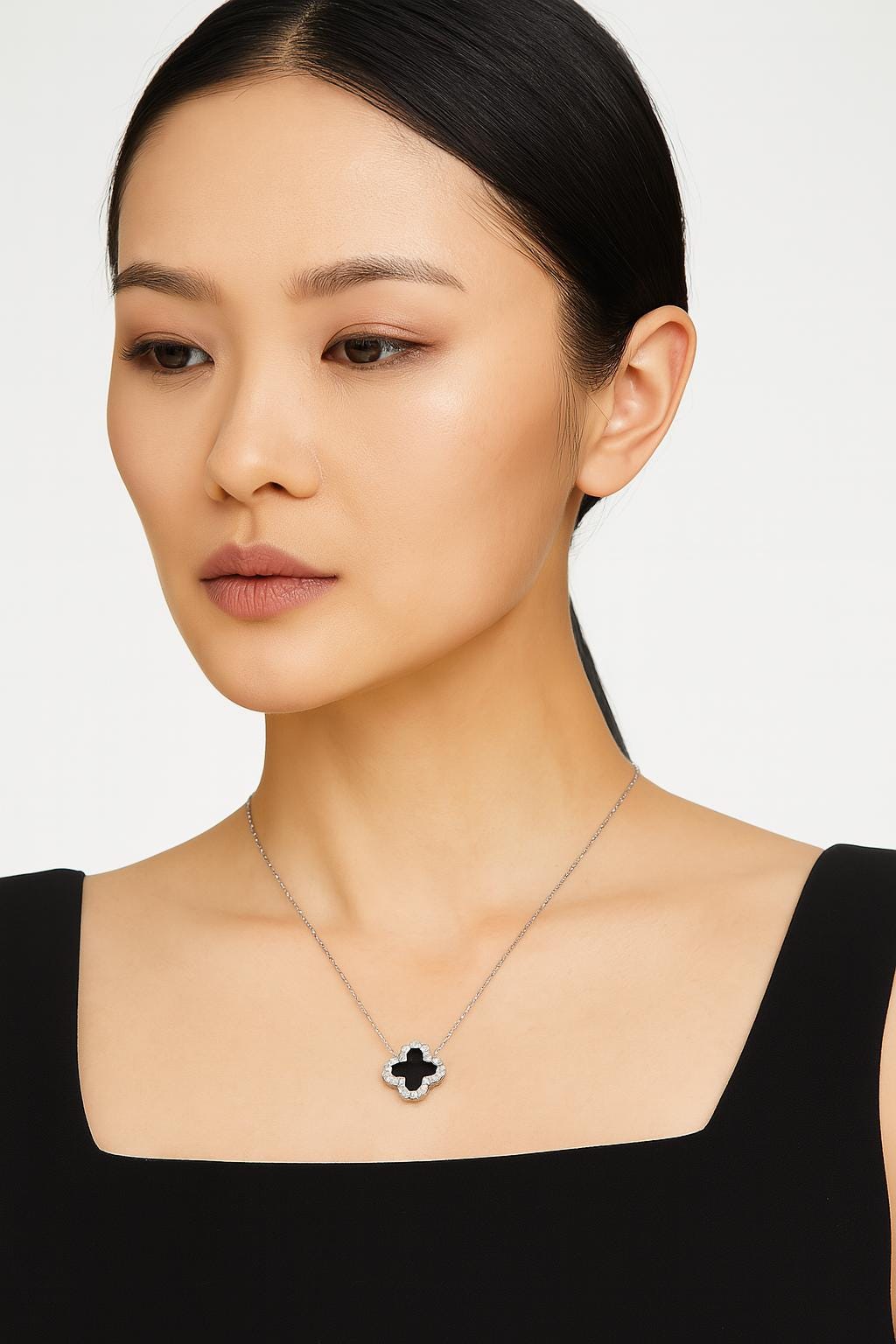 Studio photograph of a Van Cleef & Arpels necklace worn by an Asian woman in a studio setting, featuring the iconic Alhambra clover pendant with a black onyx center and diamond-studded border on a delicate white gold chain